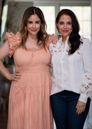 Two women smiling, one in a white shirt and the other in a pink dress, posing together.